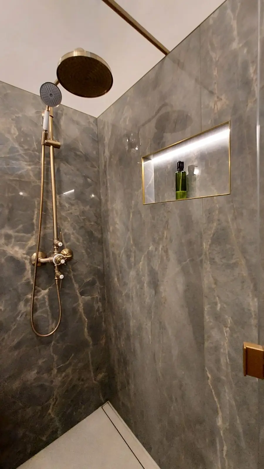 Douche en décor onyx vert brillant, robinetterie laiton doré, niche lumineuse intégrée, finitions soignées.