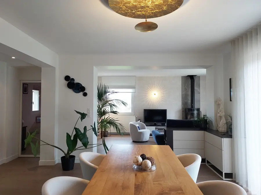 Salle à manger ouverte sur salon, table en bois massif, poêle et plantes vertes